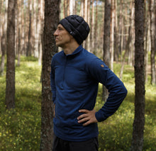 Load image into Gallery viewer, Man wearing a navy blue GOG quilted down beanie, standing in a pine forest with a hand on his hip.