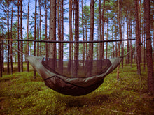 Load image into Gallery viewer, A dark brown and olive green camping hammock with an integrated black mesh mosquito net, suspended from a wooden pole in a dense pine forest.